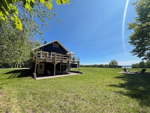 A blue house with a balcony, surrounded by a grassy field and trees.
