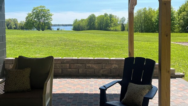 A covered patio with a view of a grassy field and a body of water.
