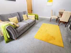 A living room with a grey sofa, yellow and green cushions, a yellow rug, and a wooden door in the background. - 17 Fairfield Road (Newcastle-upon-Tyne)