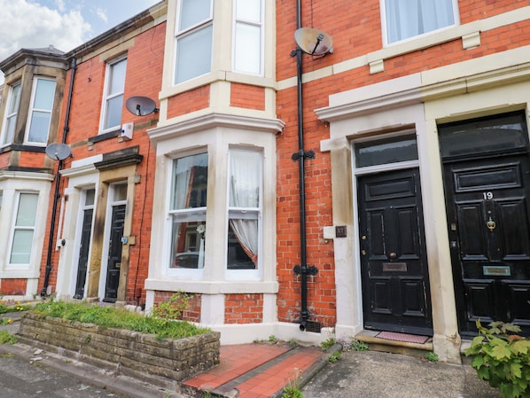 A row of red brick terraced houses with black front doors, numbered 17 and 19, and satellite dishes on the roof. - 17 Fairfield Road (Newcastle-upon-Tyne)