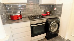 A compact kitchen with a gas stove, a red toaster, a washing machine, and grey tiled backsplash. - 17 Fairfield Road (Newcastle-upon-Tyne)