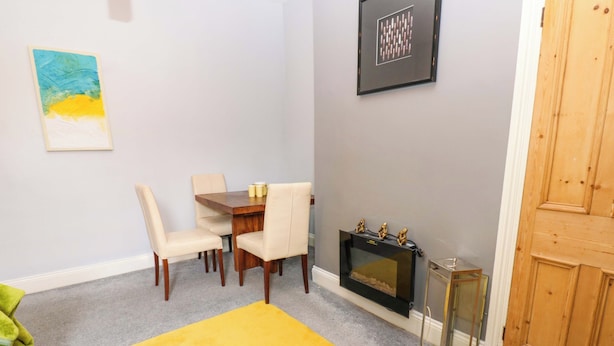 A dining area with a table and chairs, a fireplace, and a yellow rug. - 17 Fairfield Road (Newcastle-upon-Tyne)