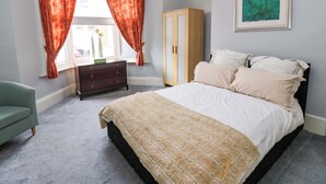 A bedroom with a bed, a dresser, a wardrobe, a chair, and a window with curtains. - 17 Fairfield Road (Newcastle-upon-Tyne)