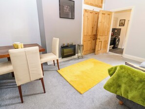 Una sala de estar con sofá, una mesa de comedor, una chimenea y una cocina visible a través de un ventanal.