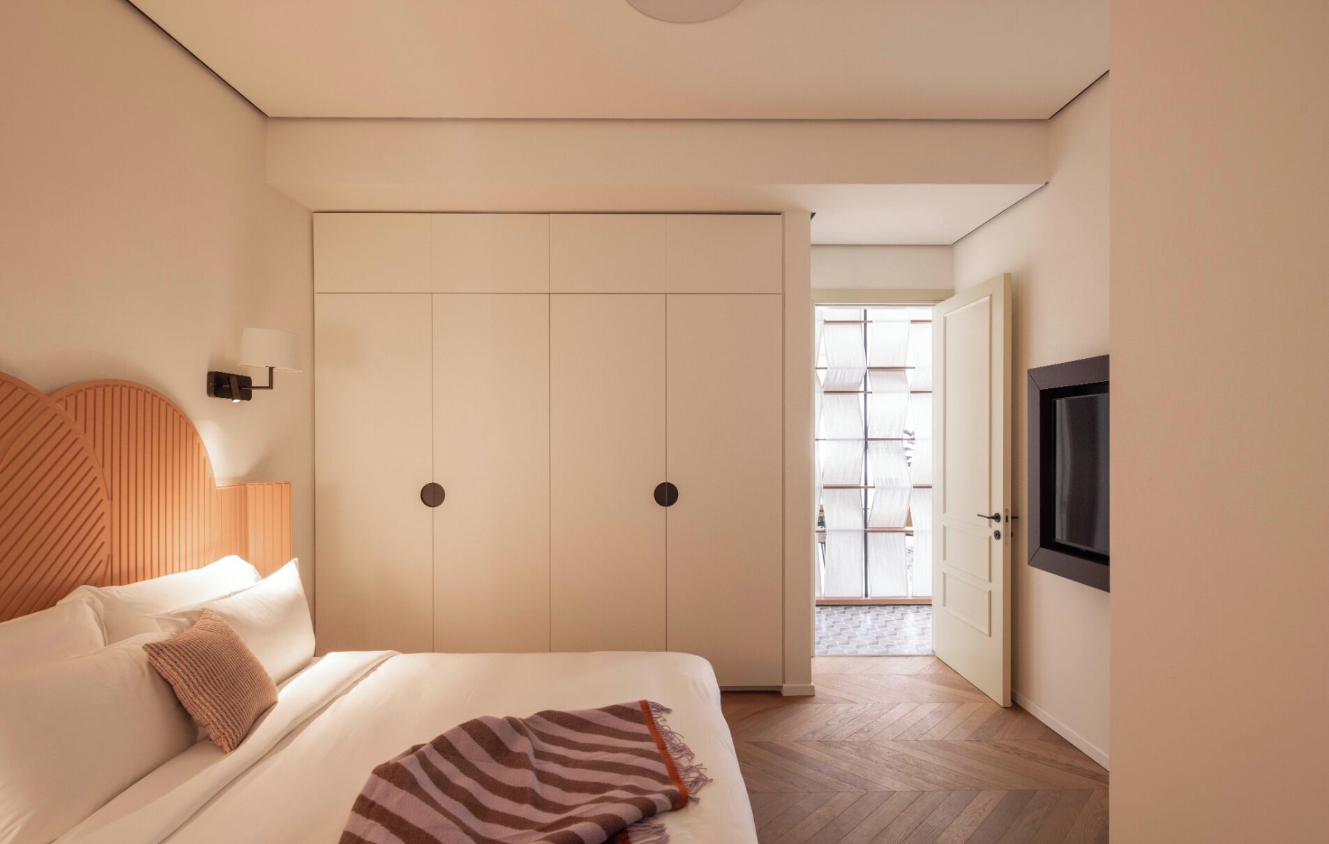Un dormitorio con cama, armario, televisión y vistas por la ventana.