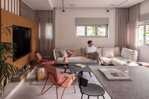 Una sala de estar moderna con un sofá, una mesa de centro, sillas, un televisor y una ventana con cortinas.