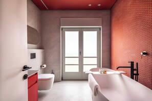 Un baño moderno con inodoro, lavabo y bañera, que cuenta con un techo rojo y un ventanal grande.