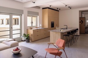 Una cocina moderna con una isla central, una zona de comedor con una mesa y sillas, y un espacio de sala de estar con un sofá y una planta.