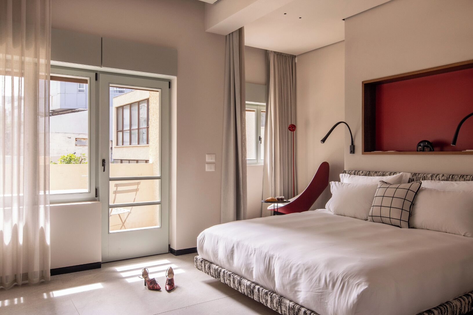 Habitación de hotel con cama, una silla, una mesa con una bebida y vista a través de una puerta corrediza.