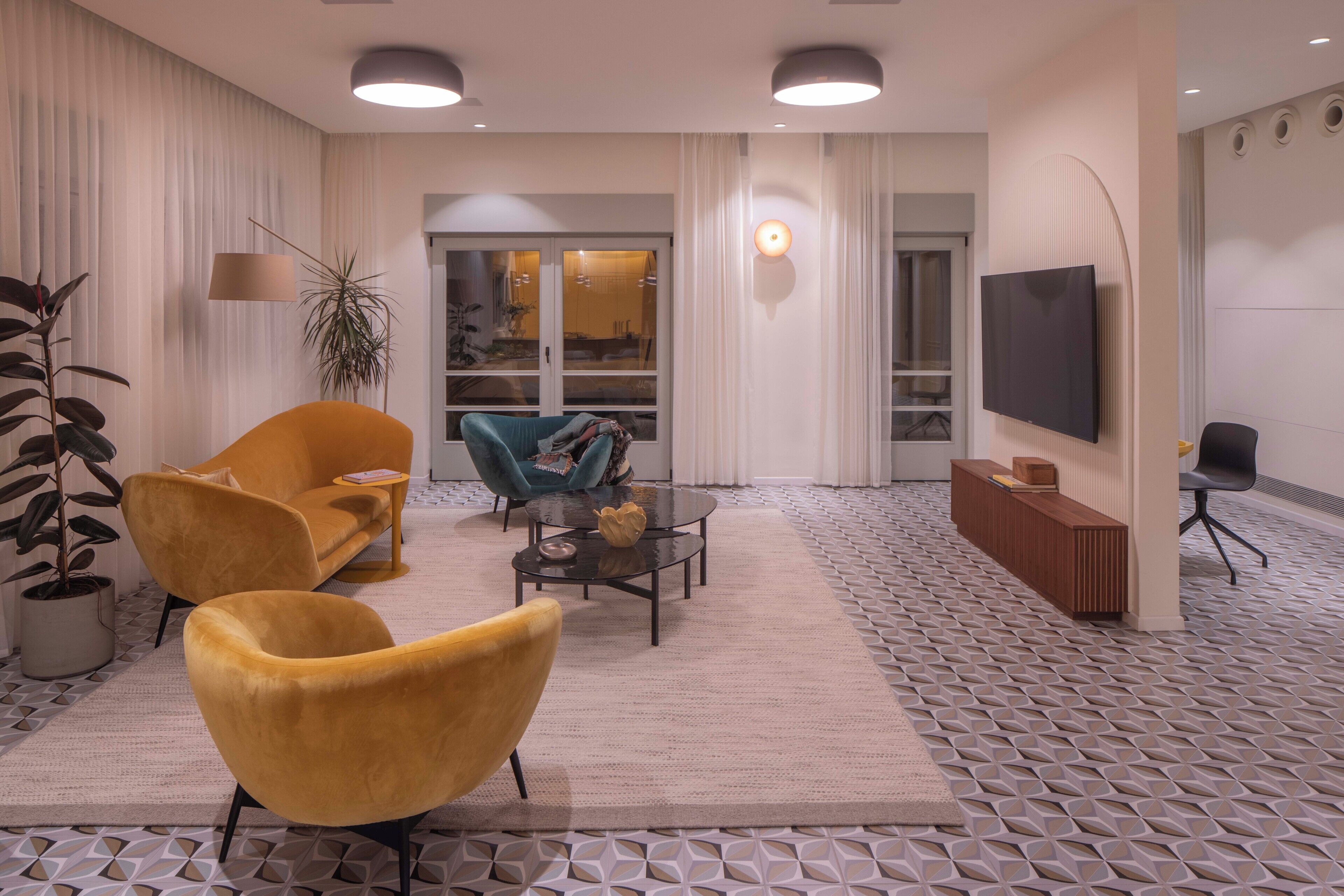 A modern living room with a sofa, two armchairs, a coffee table, a TV, and a patterned floor.