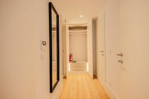 A narrow hallway with a wooden floor, a mirrored closet door, and a built-in closet with lighting. - Bonjardim Suite | Central Stay by Bolhão Market (Porto)