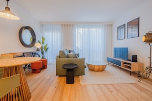 A modern living room with a sofa, coffee table, TV stand, and a dining area with a table and chairs. - Bonjardim Suite | Central Stay by Bolhão Market (Porto)