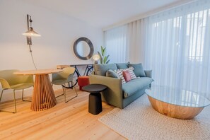 Ett modernt vardagsrum med ett runt soffbord i glas, en soffa med kuddar, ett matbord med stolar och en spegel på väggen.