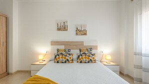 A bedroom with a large bed, two bedside tables with lamps, a wooden headboard, and two wall-mounted artworks. - Vacation Apartment 'Vivienda Carolina' with Mountain View, Shared Pool and Wi-Fi (Santa Cruz de Tenerife)