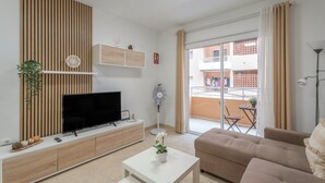 A modern living room with a flat-screen TV, a white coffee table, a beige sofa, a fan, and a balcony with a view of the city. - Vacation Apartment 'Vivienda Carolina' with Mountain View, Shared Pool and Wi-Fi (Santa Cruz de Tenerife)