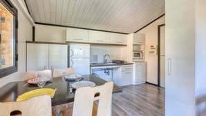 A modern kitchen with white cabinets, a dining table with chairs, and a microwave. - L'Oasis provençale - Joli chalet avec terrasse (Solliès-Toucas)