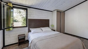 A bedroom with a bed, a small table, a window with curtains, and a wardrobe. - L'Oasis provençale - Joli chalet avec terrasse (Solliès-Toucas)