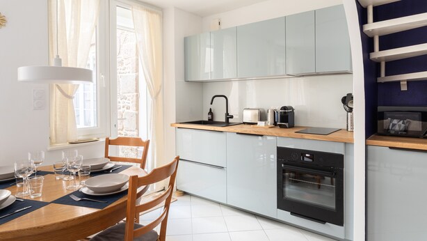 A modern kitchen with grey cabinets, a wooden dining table, and a built-in oven. - Ti Malouine - Maison dans Intra-Muros (Saint-Malo)