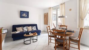 A living room with a blue sofa, a dining table with chairs, a framed picture on the wall, and a window with curtains. - Ti Malouine - Maison dans Intra-Muros (Saint-Malo)