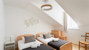 A modern bedroom with two beds, a wooden dresser, a chair, and a ceiling light fixture. - Ti Malouine - Maison dans Intra-Muros (Saint-Malo)