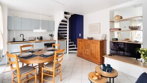 A modern kitchen with a dining area, a staircase, and a living space with a TV and decorative items. - Ti Malouine - Maison dans Intra-Muros (Saint-Malo)