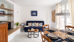 A modern living room with a blue sofa, a dining table set for four, and a kitchen area with wooden shelves. - Ti Malouine - Maison dans Intra-Muros (Saint-Malo)