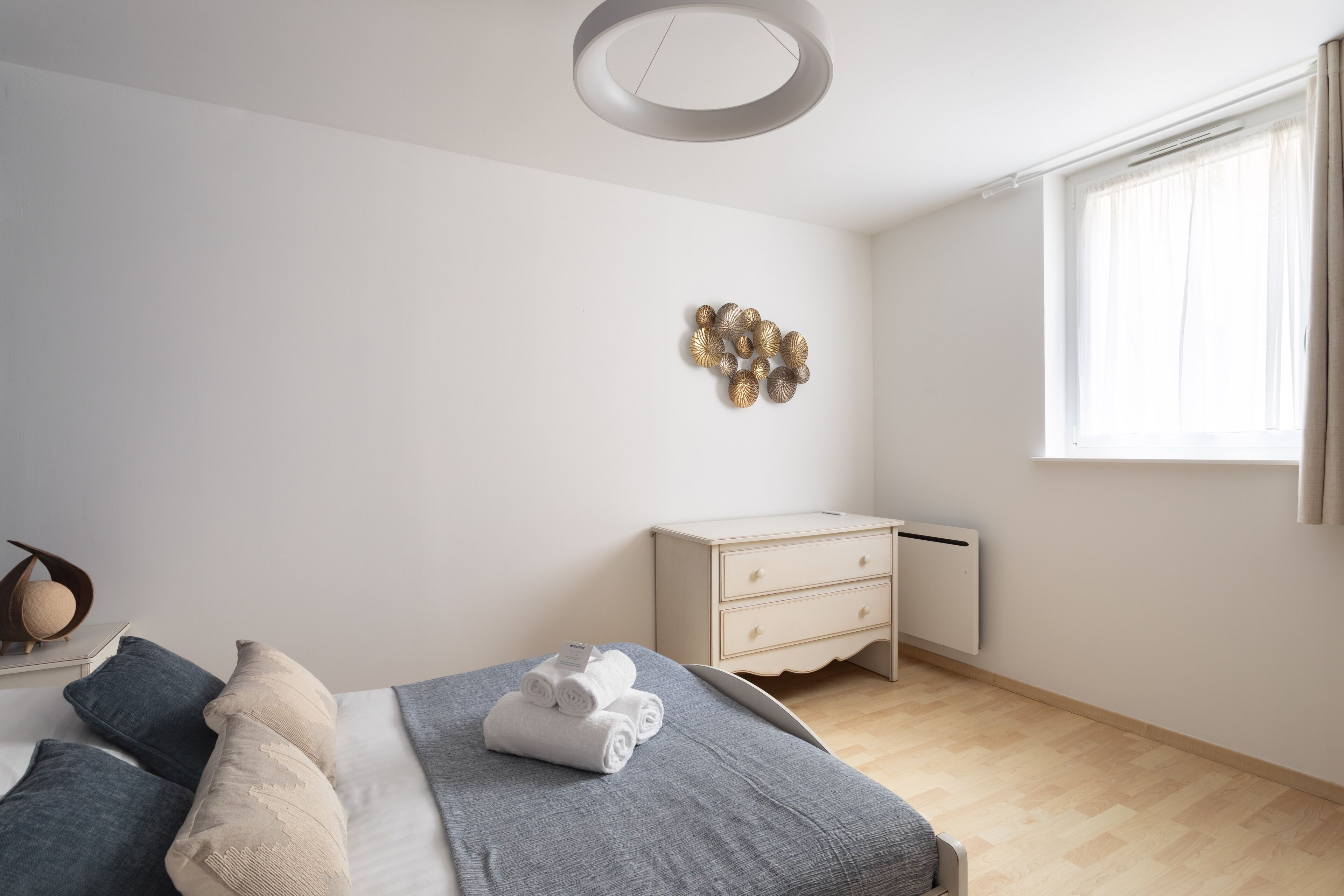 A bedroom with a bed, bedside table, dresser, and a decorative wall piece.