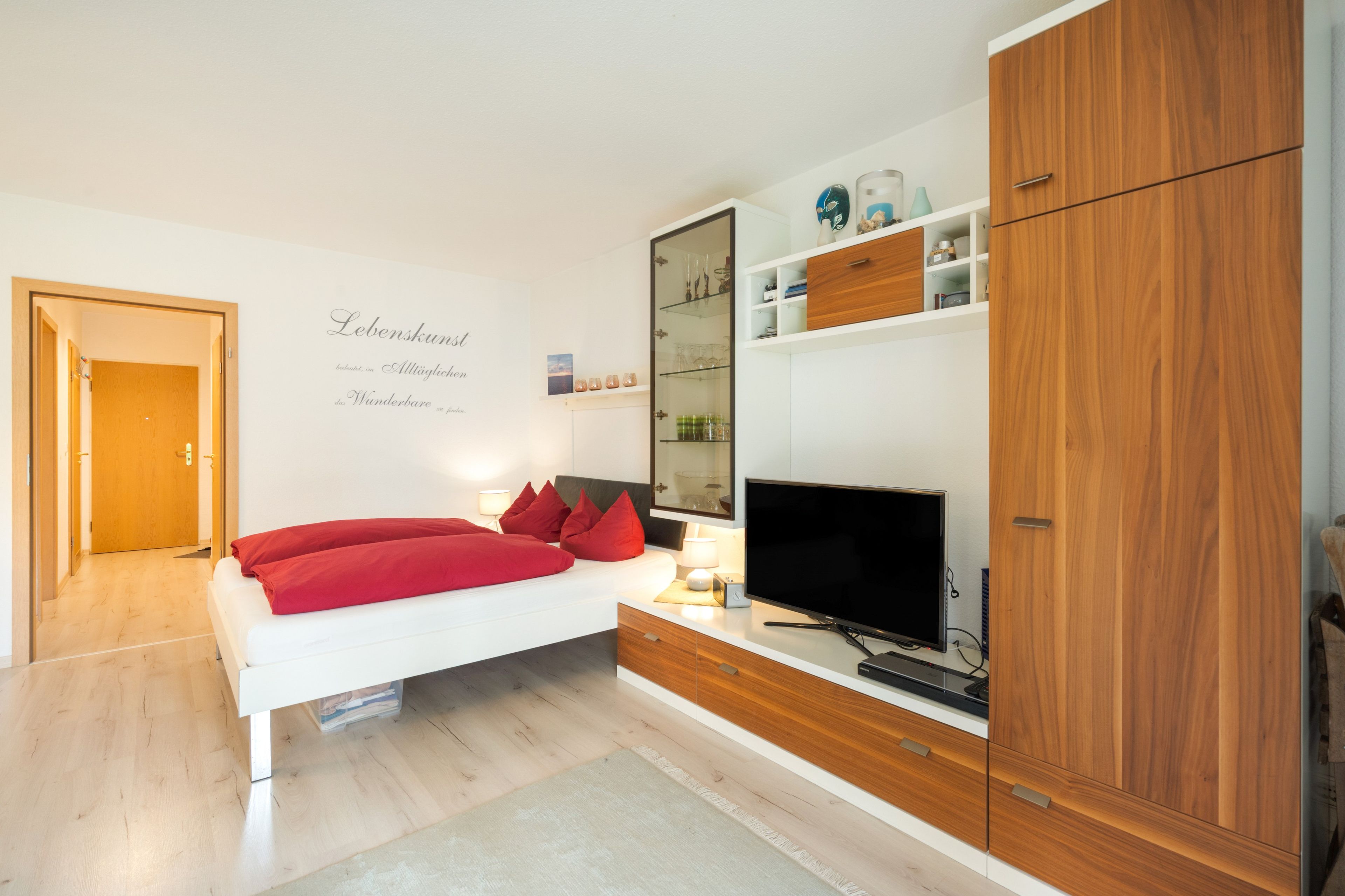Ein modernes Schlafzimmer mit einem Bett, einem Fernseher, Holzschränken und einer Wand mit Text.