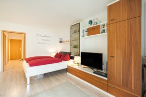 A modern bedroom with a bed, a TV, wooden cabinets, and a wall with text. - Elbappartement Dresden – Modern Apartment Near the Elbe with Terrace and Garden Access (Dresden)