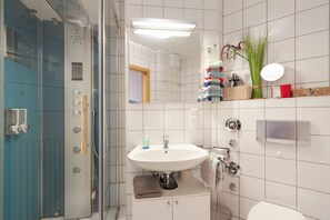 A bathroom with a glass shower enclosure, a white sink, a mirror, and a towel rack. - Elbappartement Dresden – Modern Apartment Near the Elbe with Terrace and Garden Access (Dresden)