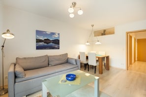 Un salon moderne avec un canapé gris, une table basse en verre et un coin repas comprenant une table et des chaises en bois.