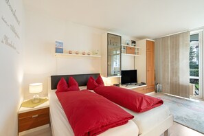 A hotel room with a bed, bedside tables, a TV, a wardrobe, and a large window. - Elbappartement Dresden – Modern Apartment Near the Elbe with Terrace and Garden Access (Dresden)