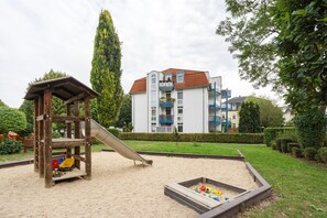 A playground with a slide and climbing structures, surrounded by a well-maintained garden and a multi-story residential building in the background. - Elbappartement Dresden – Modern Apartment Near the Elbe with Terrace and Garden Access (Dresden)