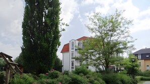 A pathway leading to a building with a red roof, surrounded by lush greenery and flowering bushes. - Elbappartement Dresden – Modern Apartment Near the Elbe with Terrace and Garden Access (Dresden)