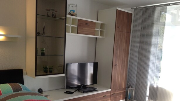 A bedroom with a bed, a TV, a wardrobe, and a window with blinds. - Elbappartement Dresden – Modern Apartment Near the Elbe with Terrace and Garden Access (Dresden)