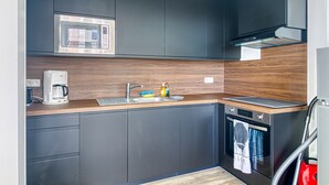 A modern kitchen with dark cabinets, a microwave, a coffee maker, and a built-in oven. - L’Attitude Mer - À 20 m de la plage (Bray-Dunes)
