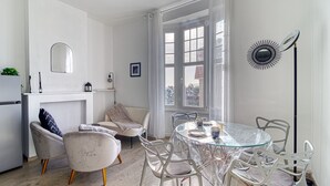 A modern kitchen with a built-in oven, a dining area with a glass table and white chairs, and a large window with curtains. - L’Attitude Mer - À 20 m de la plage (Bray-Dunes)