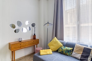 Una sala de estar moderna con sofá, cojines, una consola de madera y espejos en la pared.