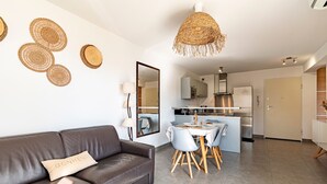 Ett modernt vardagsrum med en brun lädersoffa, ett runt soffbord i glas och en matplats med ett vitt bord och blå stolar.