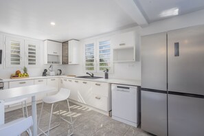 Eine moderne Küche mit weißen Schränken, einem Edelstahlkühlschrank, einer Spülmaschine und einem Fenster mit Blick auf Grünflächen.