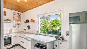 Una cocina moderna con armarios blancos, horno integrado, un amplio ventanal con vistas a zonas verdes y un refrigerador de acero inoxidable.