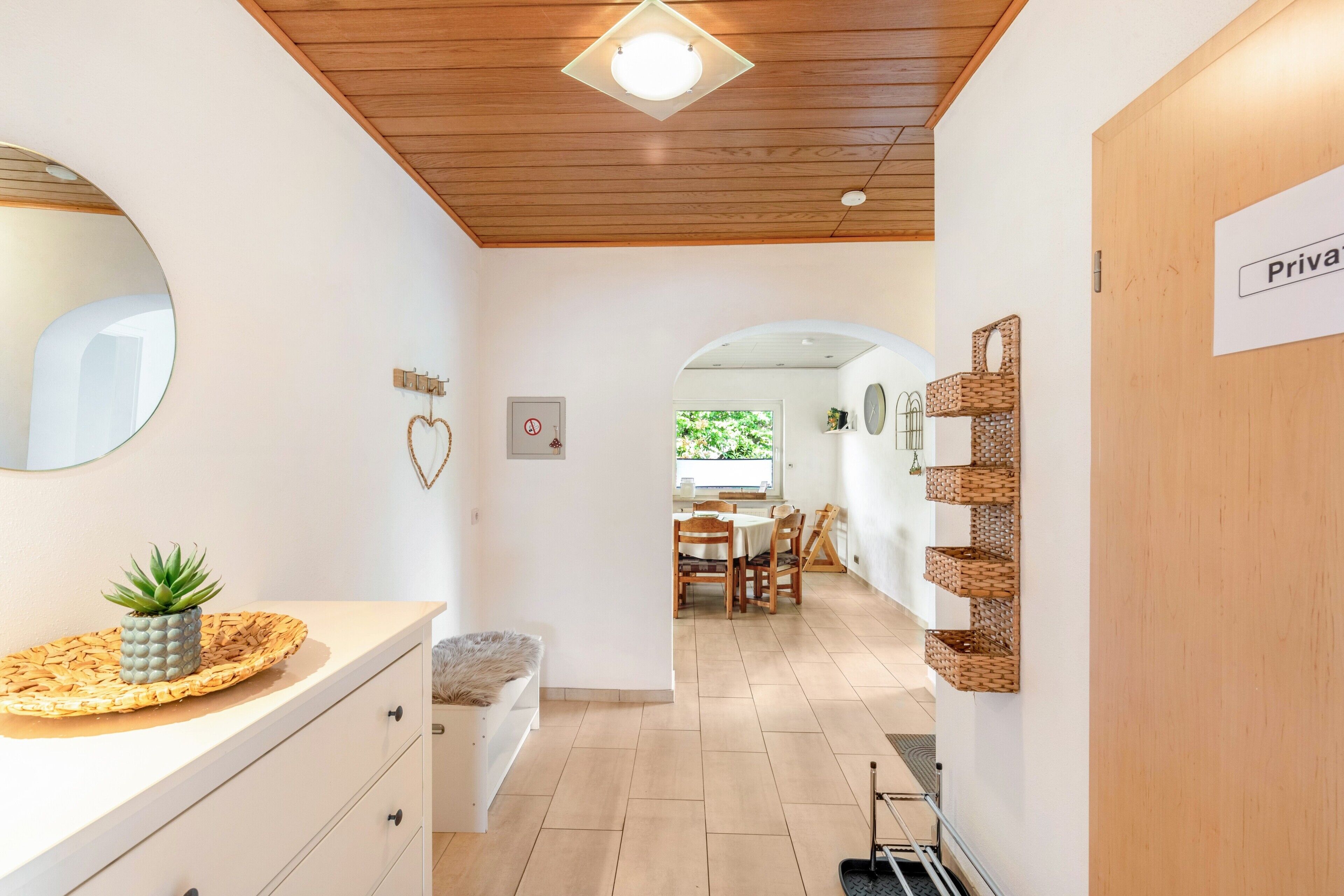 Un pasillo con techo de madera, un espejo, una planta pequeña, un aparador blanco, una zona de comedor con mesa y sillas, y un cartel que dice 'Private'.