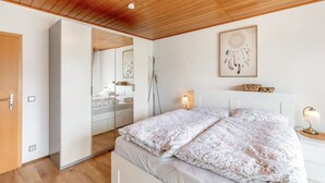 Un dormitorio con techo de madera, una cama con ropa de cama floral, una mesita de noche con lámpara, un espejo y un atrapasueños en la pared.