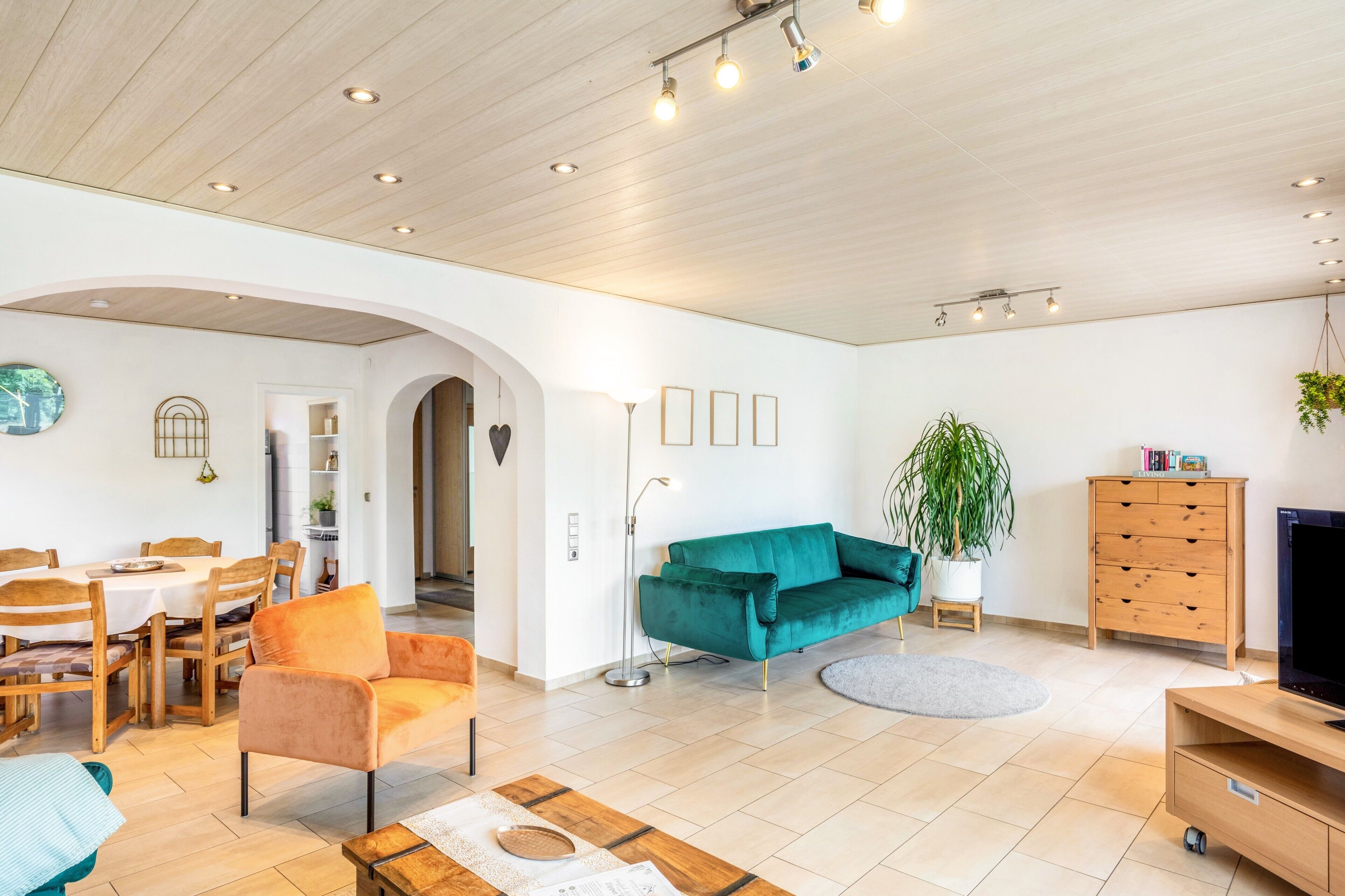 A modern living room with a dining area, wooden ceiling, and a TV stand.