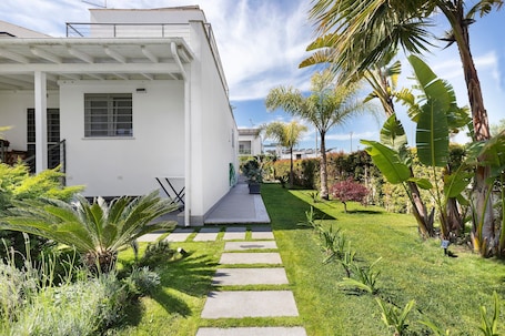 A modern house with a paved pathway leading to the entrance, surrounded by lush greenery and palm trees.. Holiday Home 'Zampamare Bb - Anzio' with Private Terrace, Private Garden and Wi-Fi