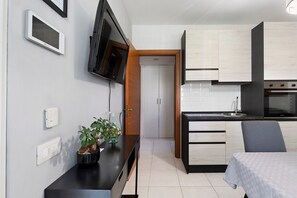 Una cocina moderna con horno empotrado, un comedor con mesa y sillas, y un televisor montado en la pared.
