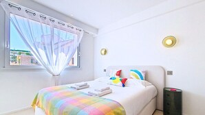 A bedroom with a bed, a window with curtains, a bedside lamp, and a nightstand. - N&J - STUDIO ANNA - Central Nice • AC • Walk to beach (Nice)
