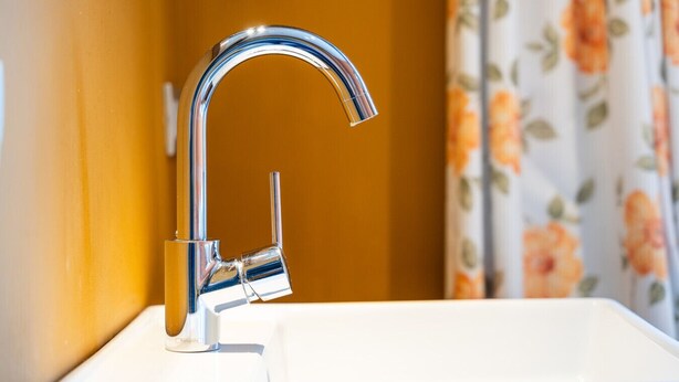 Une salle de bain avec un robinet chromé, un lavabo blanc et des rideaux à motifs floraux.