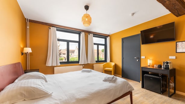 Hotellihuone, jossa on sänky, työpöytä, tuoli, televisio ja ikkuna, jossa on verhot.