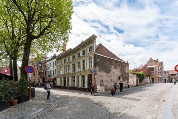 En kullerstensgata med historiska byggnader, en parkeringsförbudsskylt och fotgängare.